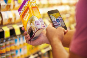 Man Scanning Voucher Code In Supermarket With Mobile Phone
